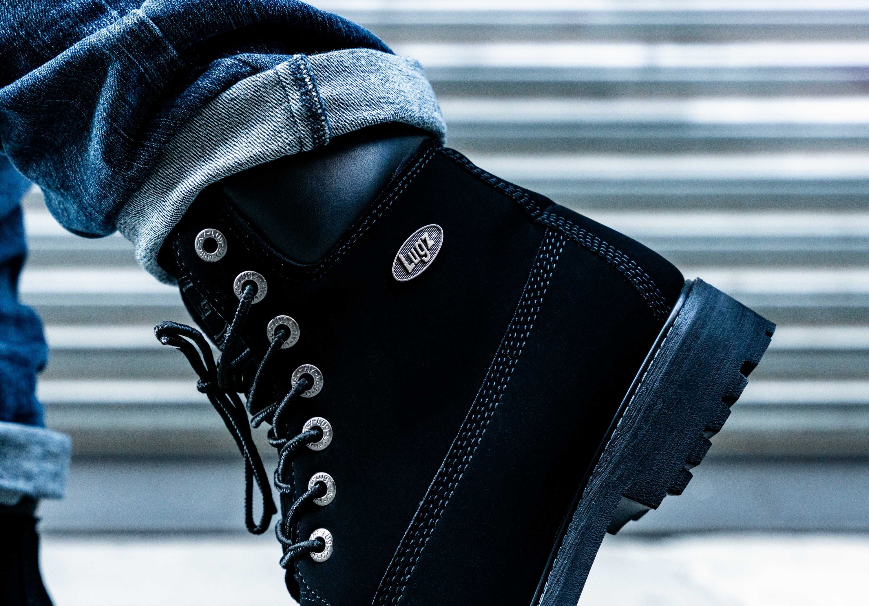 Black boot with brand logo worn by a person, against a blurred background