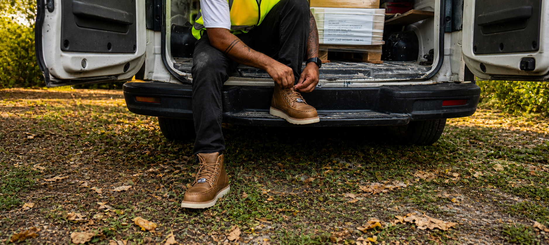 Person sitting on a van with a box, wearing brown boots and a high-visibility vest.