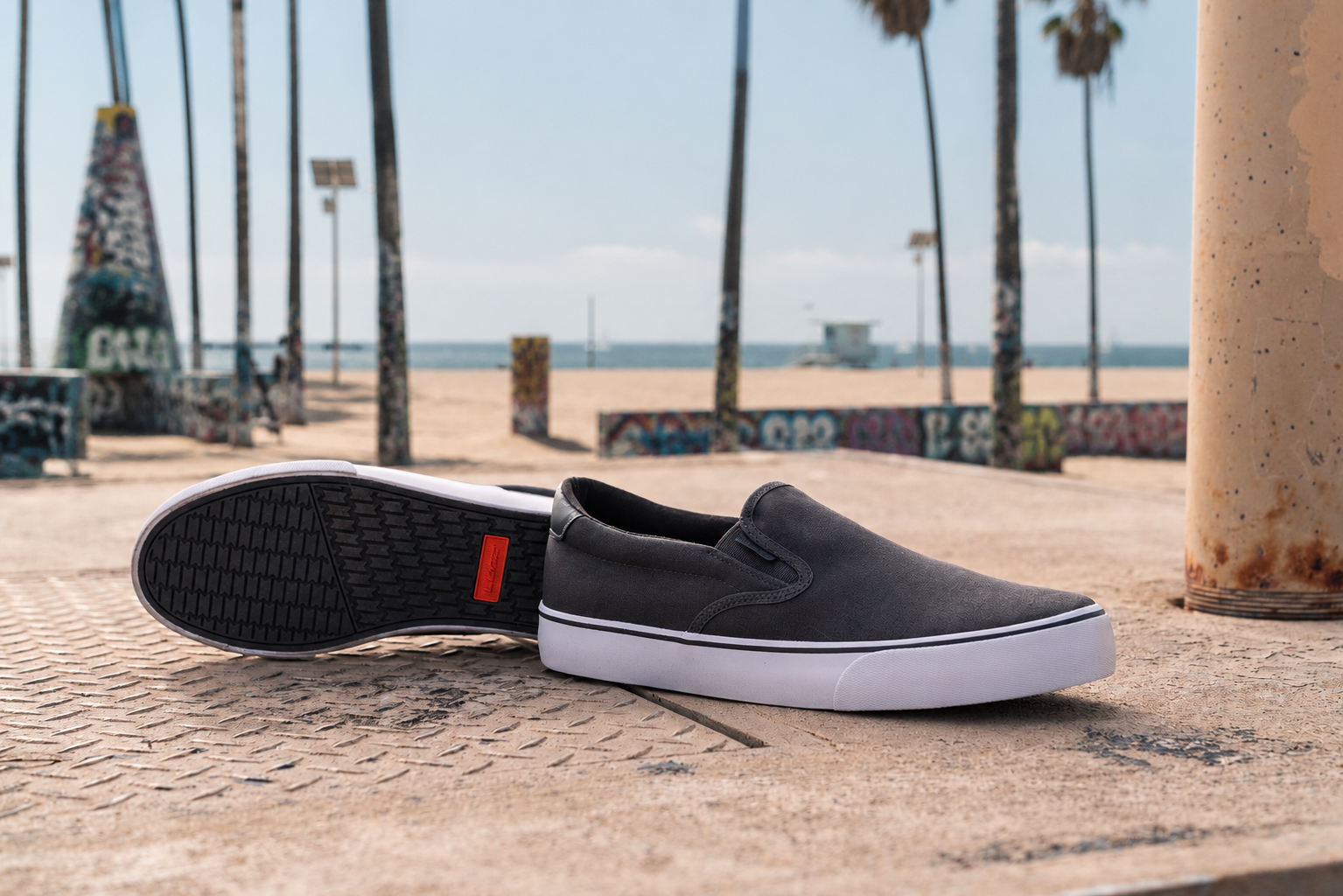 Dark Grey slip-on shoes on a textured surface with palm trees and beach in the background